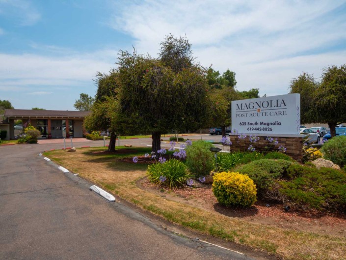 A view of a motel entrance with a sign, surrounded by landscaped greenery and trees.