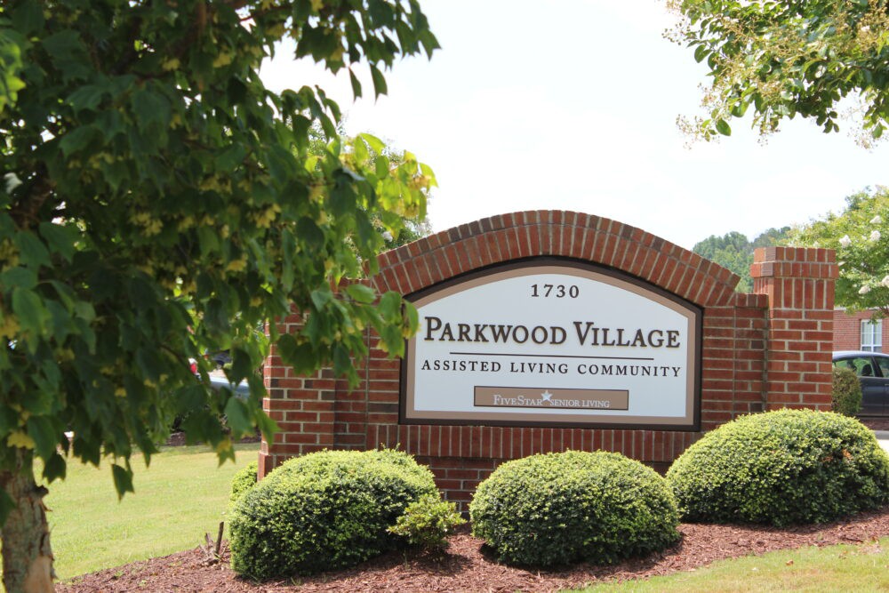 Entrance sign for Parkwood Village Assisted Living Community surrounded by well-maintained greenery.