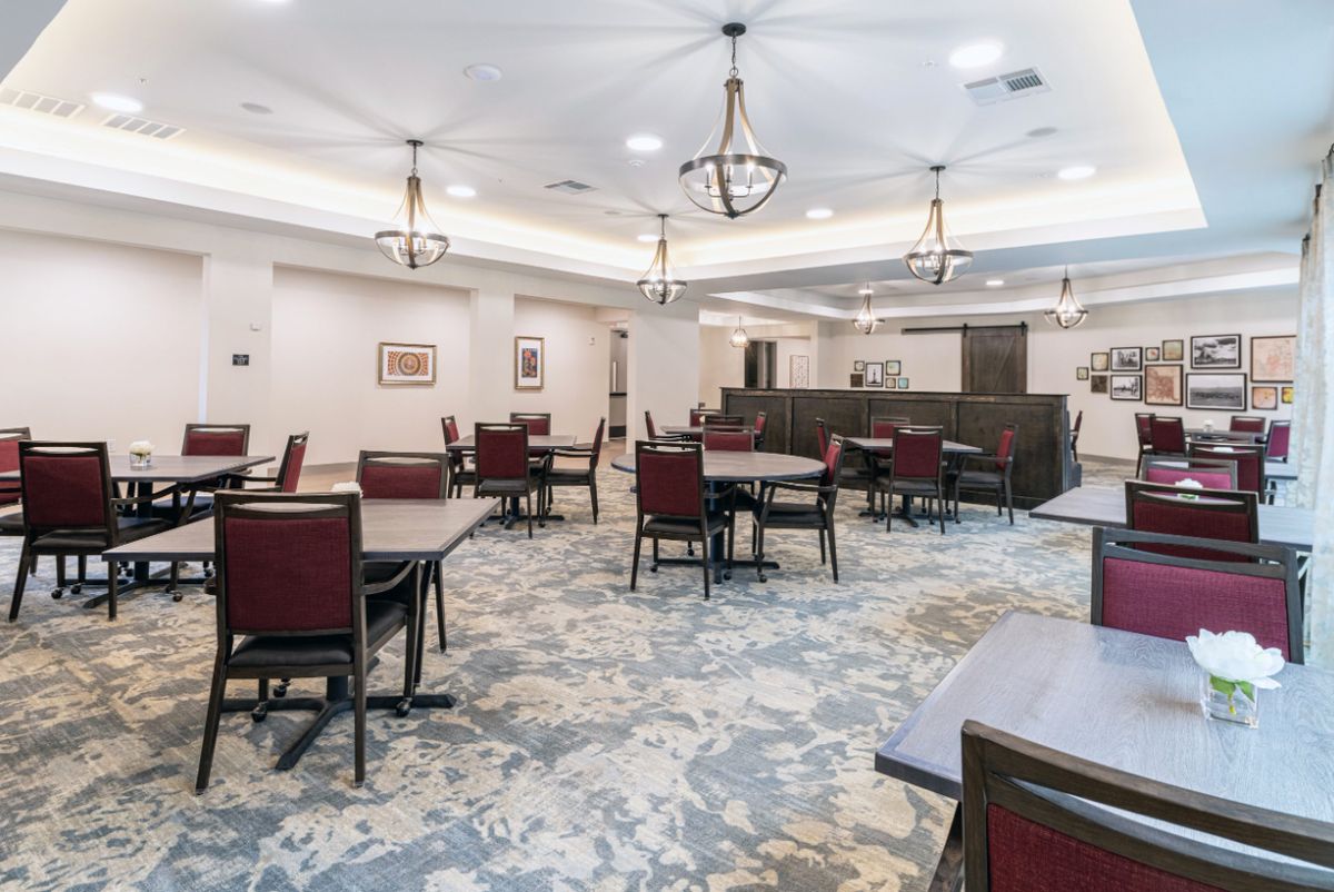 Spacious dining area with neatly arranged tables and chairs, featuring elegant chandeliers and a patterned carpet.