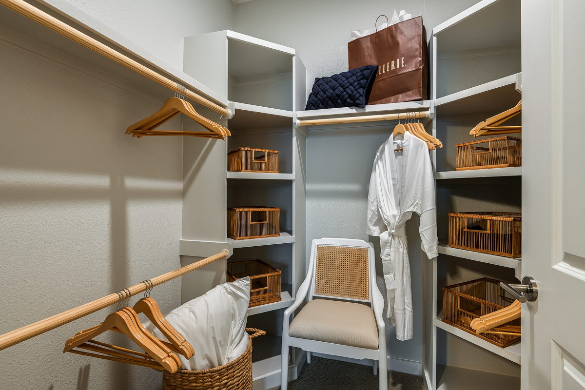 A neatly organized walk-in closet featuring wooden hangers, storage baskets, and a white bathrobe hanging on display.