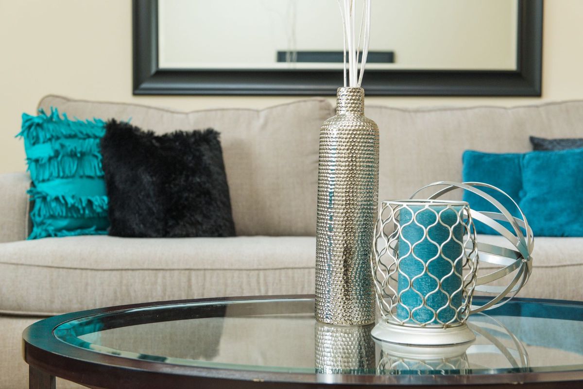 A stylish living room featuring a sofa with decorative cushions, a sleek vase, and a candle holder on a glass table.