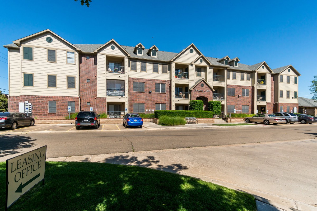 A suburban apartment building with a parking lot and cars in front.