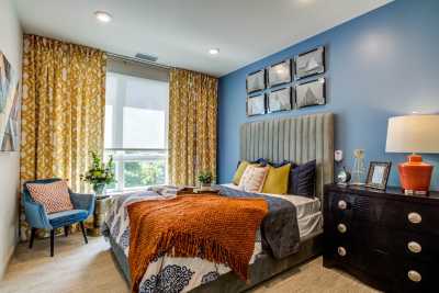 A cozy and stylish bedroom with blue walls, a king-size bed adorned with colorful pillows and a throw blanket, complemented by elegant curtains and a nightstand.