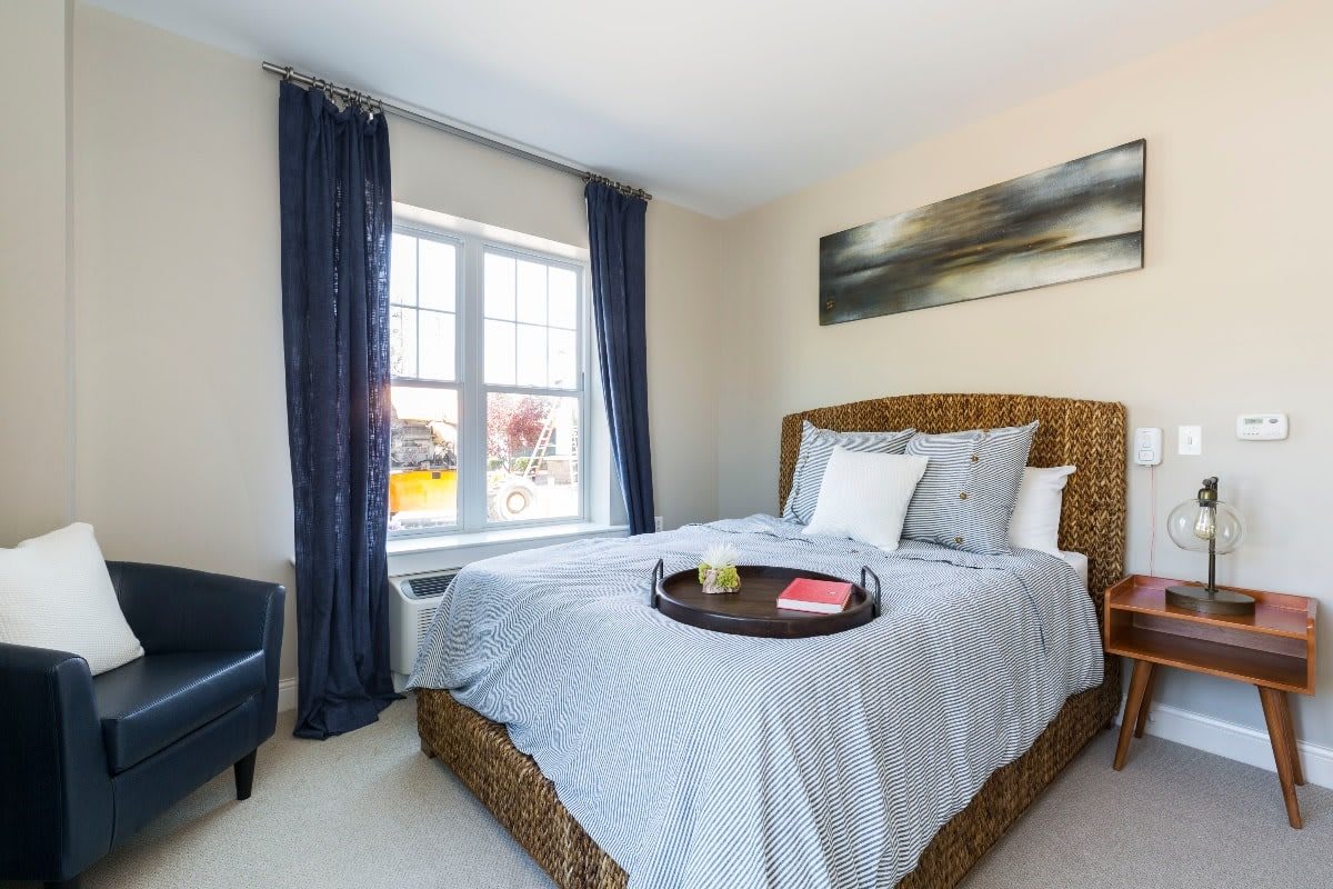 A cozy, modern bedroom with a wicker bedframe, blue curtains, and a tray on the neatly made bed.