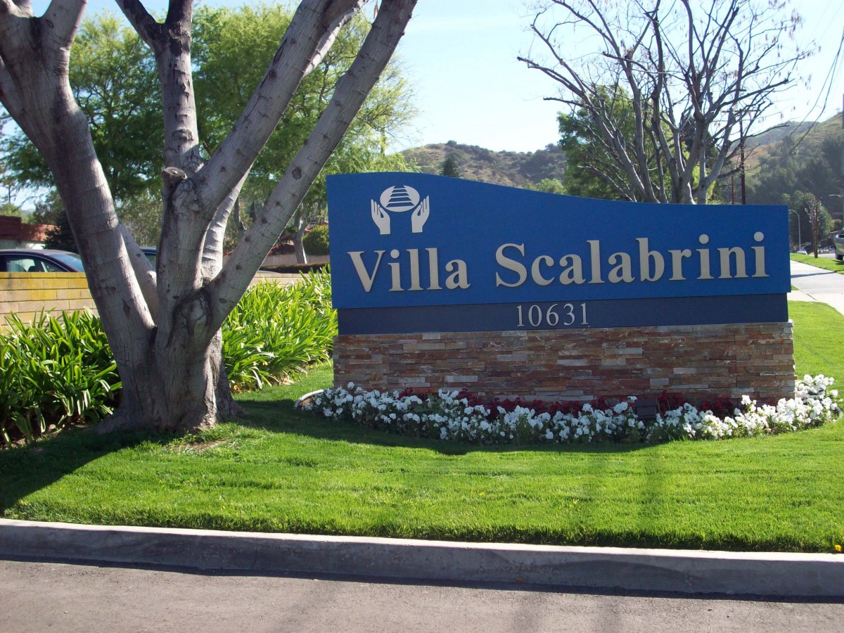 Entrance sign for Villa Scalabrini surrounded by trees and landscaping.
