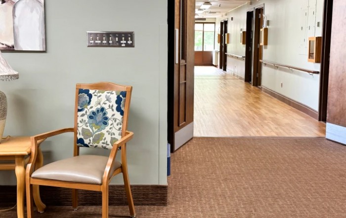 A hallway with a wooden chair featuring a floral cushion and visible signage on the wall.