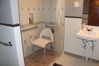 An accessible bathroom with a shower chair and grab bars for safety.