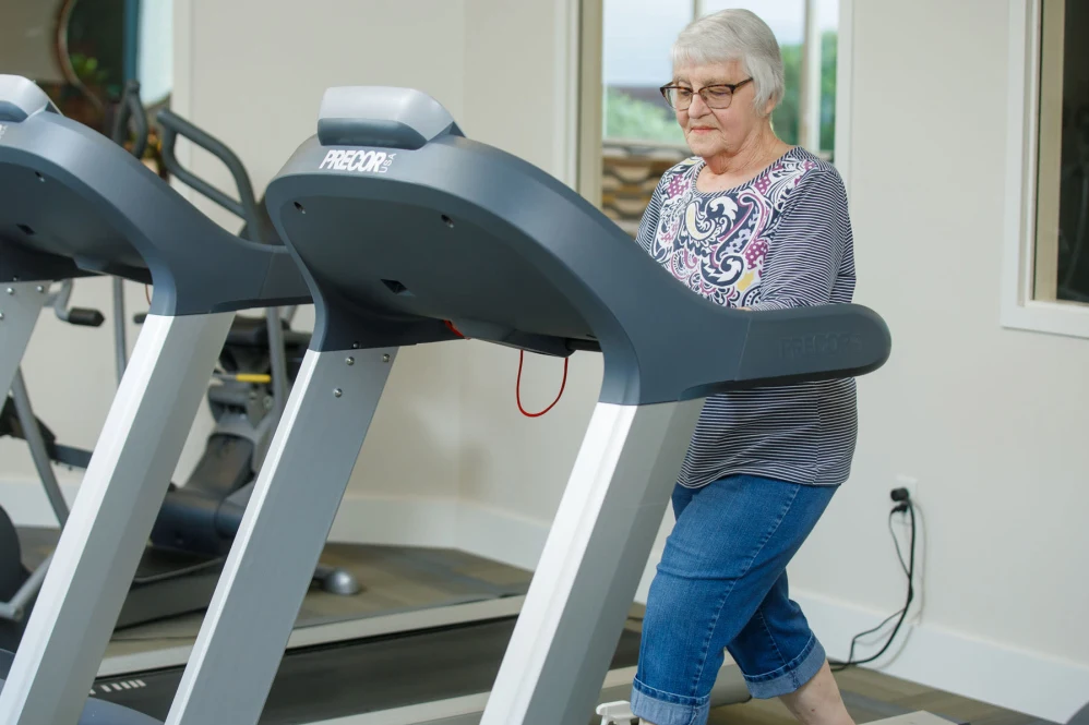 An elderly woman exercising on a treadmill in a gym setting.
