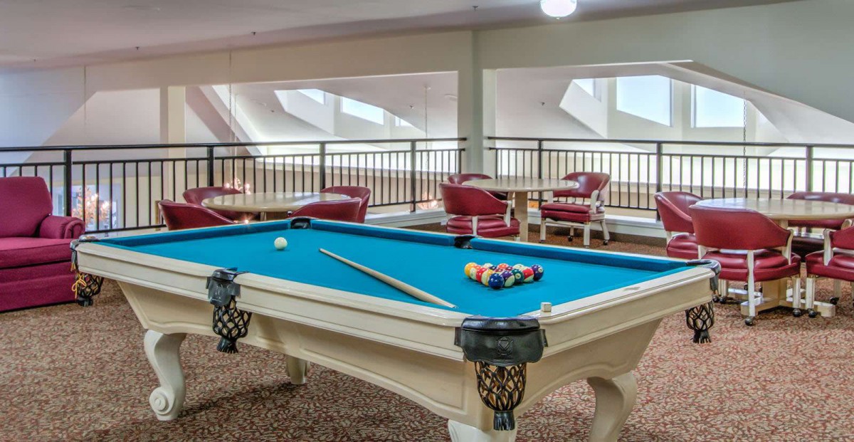 A stylish game room featuring a blue-felt pool table with cues and balls ready for play, surrounded by comfortable seating.