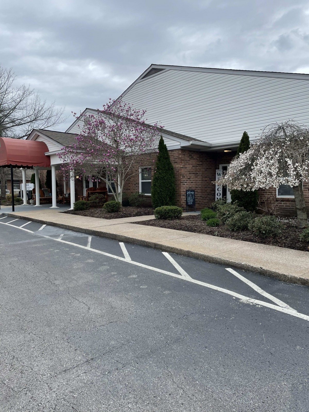A building with a covered entrance and adjacent parking area on a cloudy day.