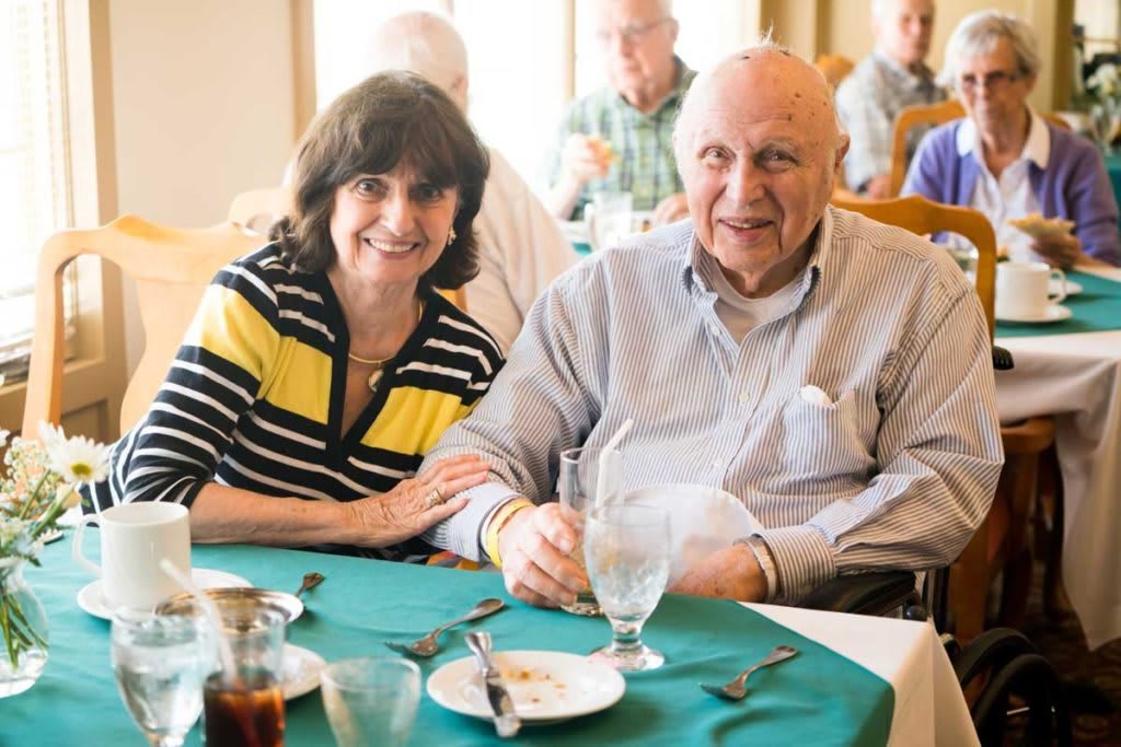 A couple smiling while seated at a dining table in a restaurant.