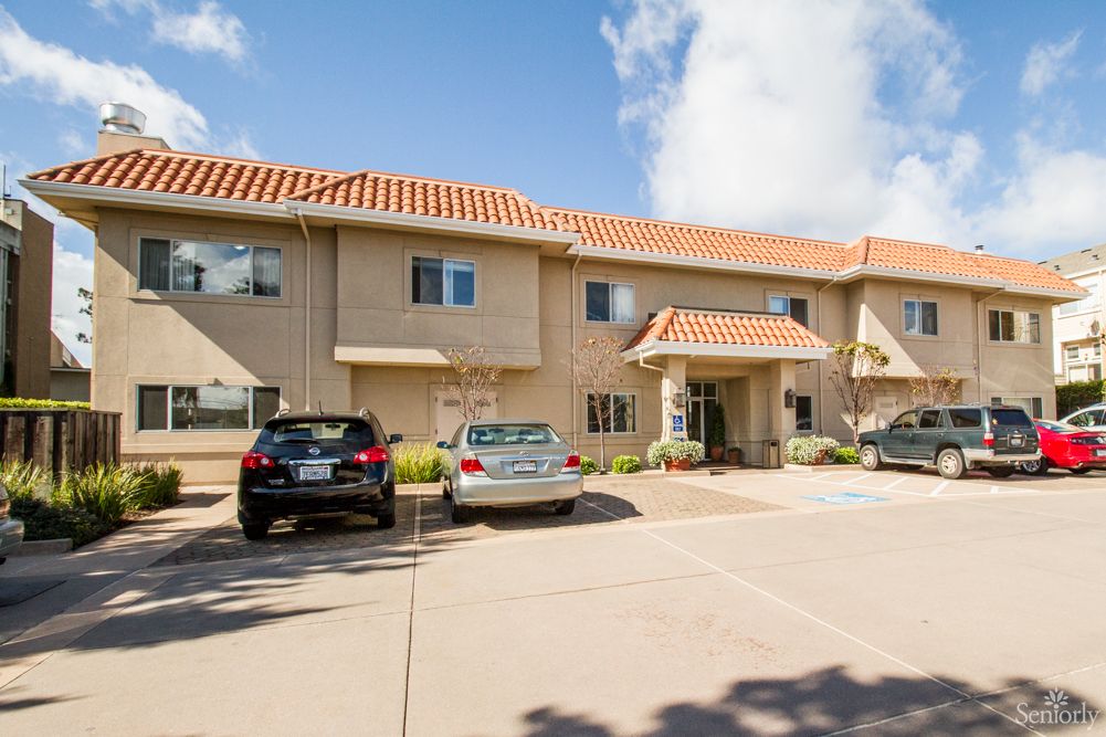 A two-story apartment building with a small parking lot in front, featuring several parked cars.