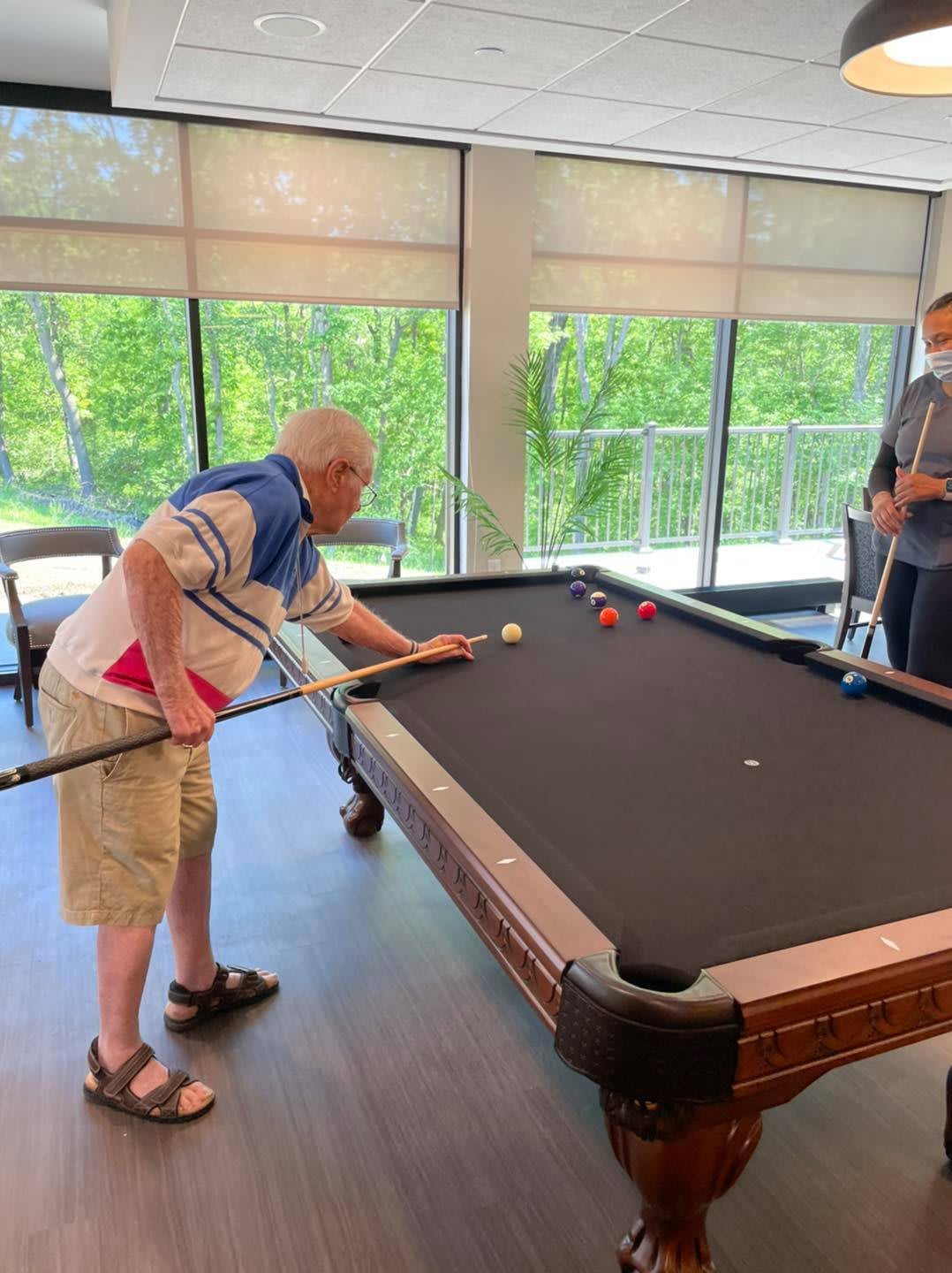 An elderly man plays billiards in a well-lit room.