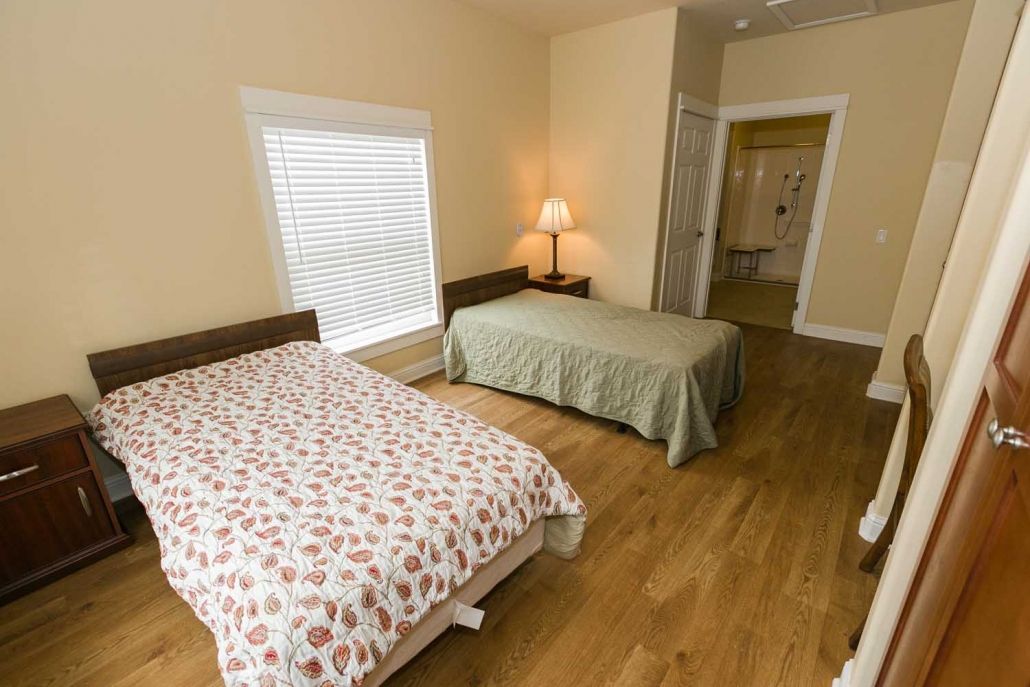 A cozy bedroom featuring two beds with a lamp and wooden flooring.