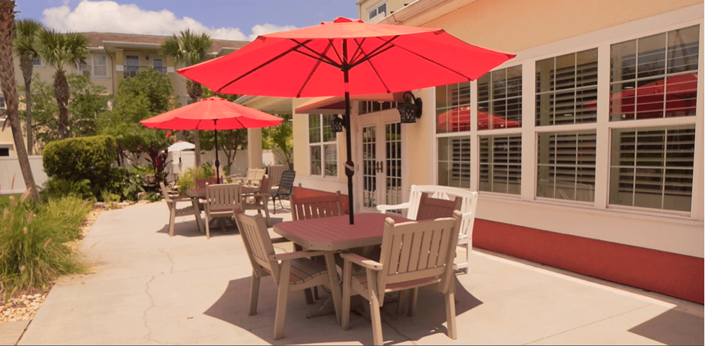 A sunny patio with tables and red umbrellas.