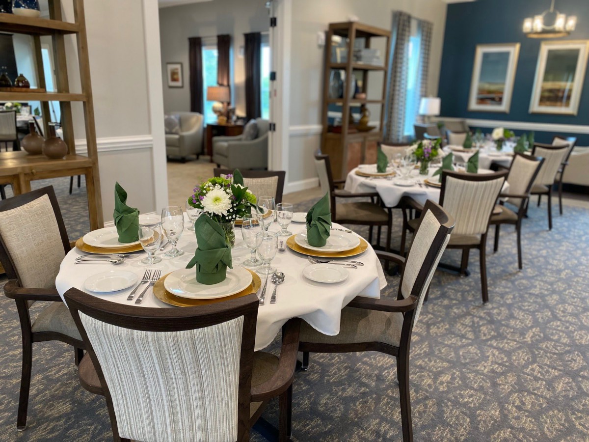 A sophisticated dining room with elegantly set tables, featuring folded napkins and floral centerpieces.