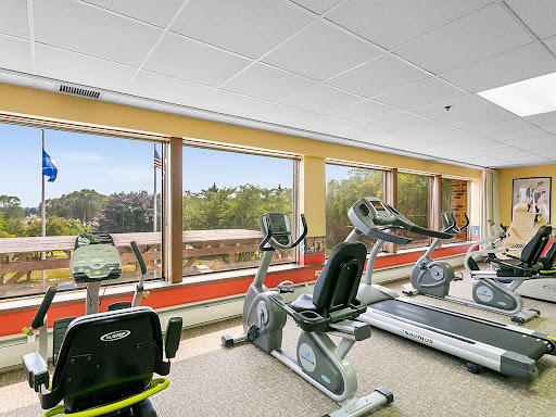A modern fitness center with various exercise equipment and large windows allowing natural light.