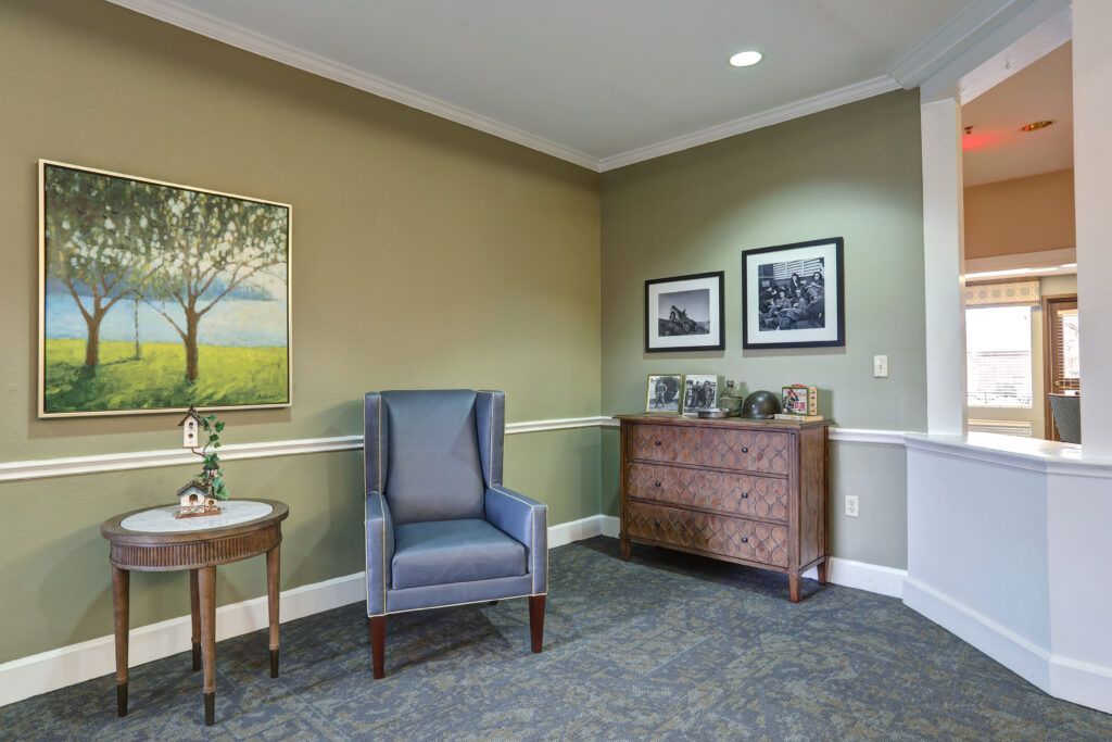 A cozy living room corner featuring an armchair, side table, and a wooden dresser with framed photos and artwork on the walls.