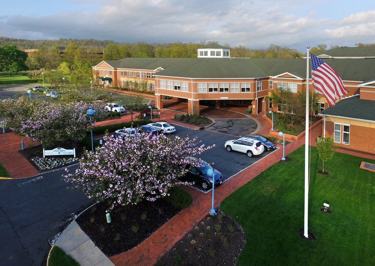 Aerial view of a brick building with a parking lot, trees, and an American flag in the foreground.