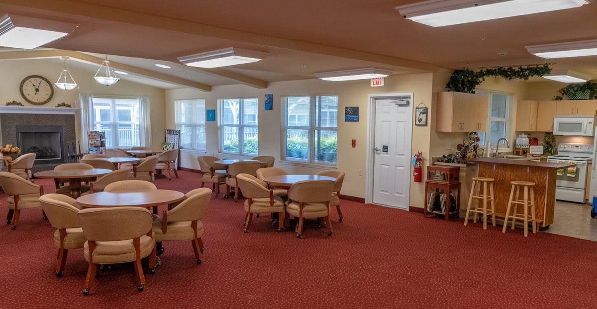 A spacious dining area with multiple tables and chairs, featuring large windows and a red carpet.