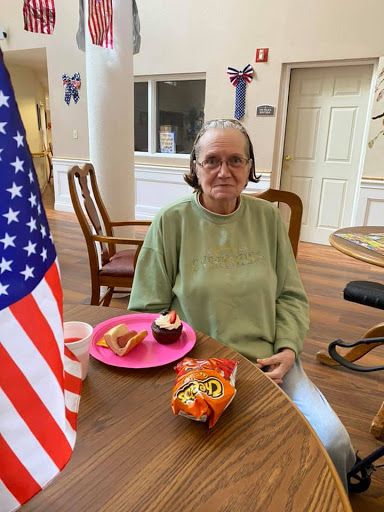 An elderly individual enjoys snacks in a cheerful setting, accompanied by an American flag.