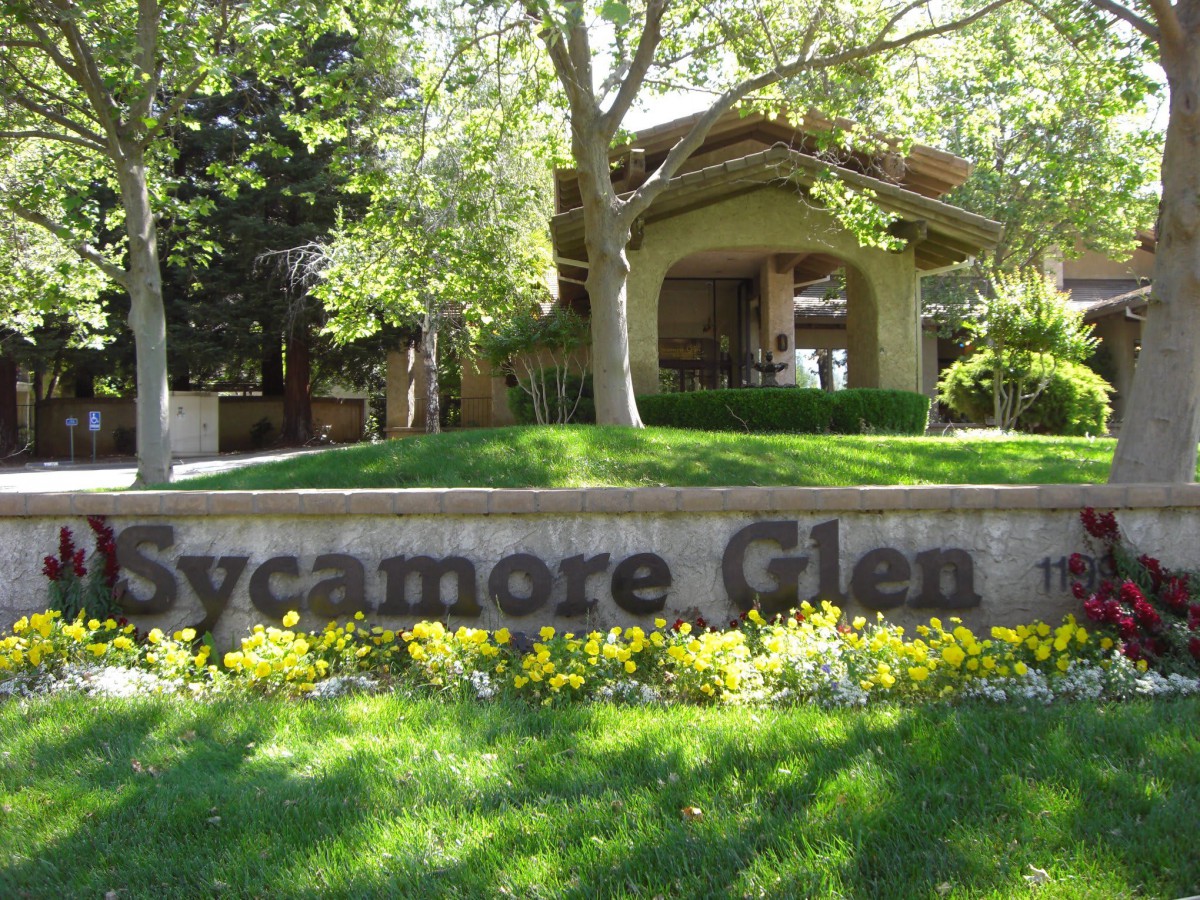 A welcoming entrance to Sycamore Glen surrounded by lush greenery and trees.