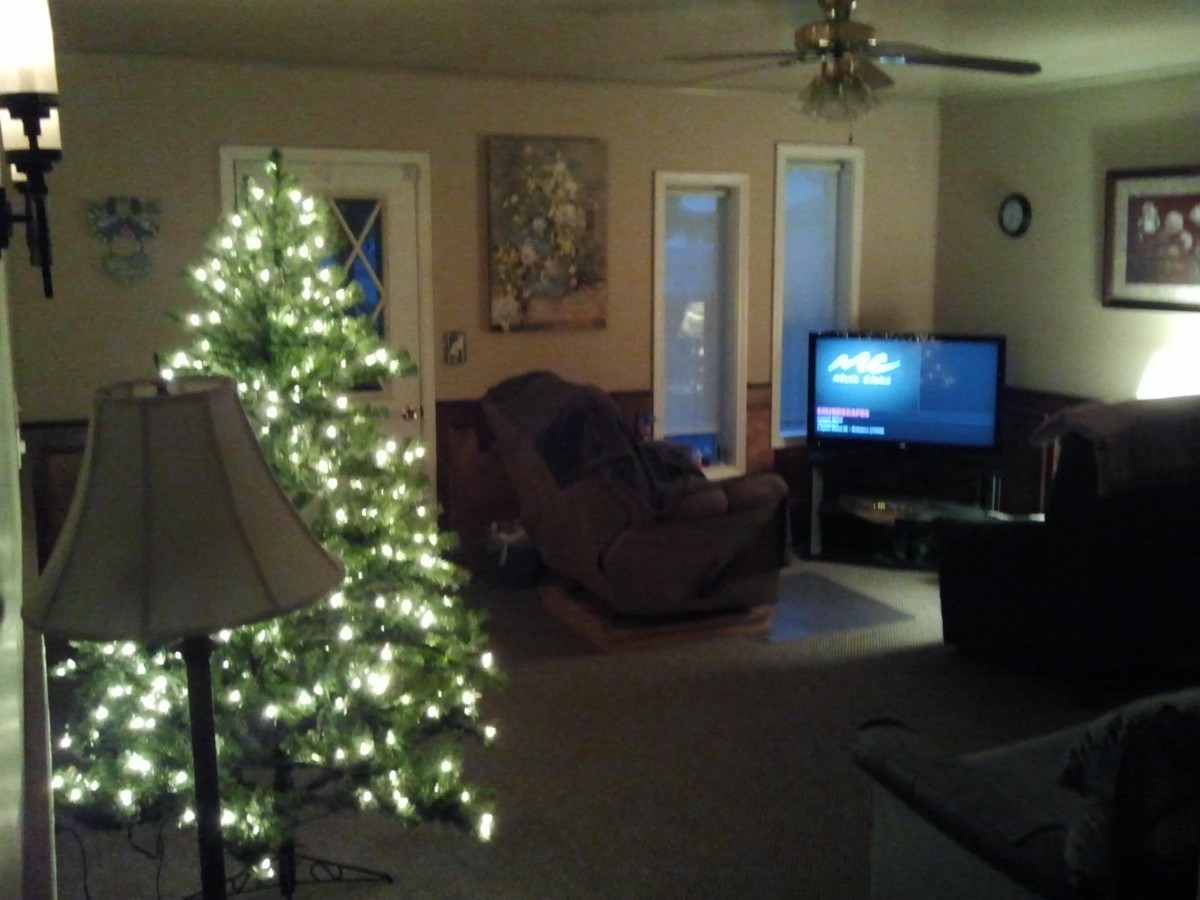 A cozy living room with a lit Christmas tree, armchair, and television.