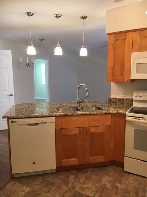 A modern kitchen interior with granite countertops and wood cabinets.