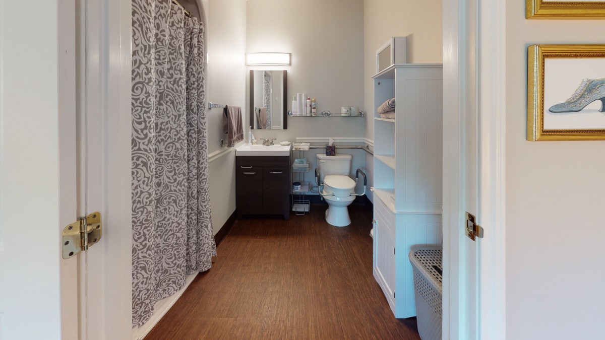 A modern bathroom featuring a shower with a patterned curtain, toilet, sink with a vanity, and ample storage shelving.