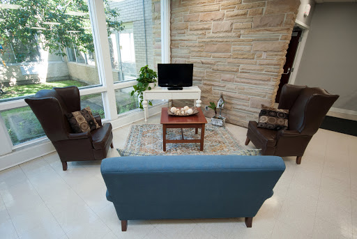 A cozy living room setup featuring a blue sofa, brown chairs, a small table, and a television against a backdrop of large windows.