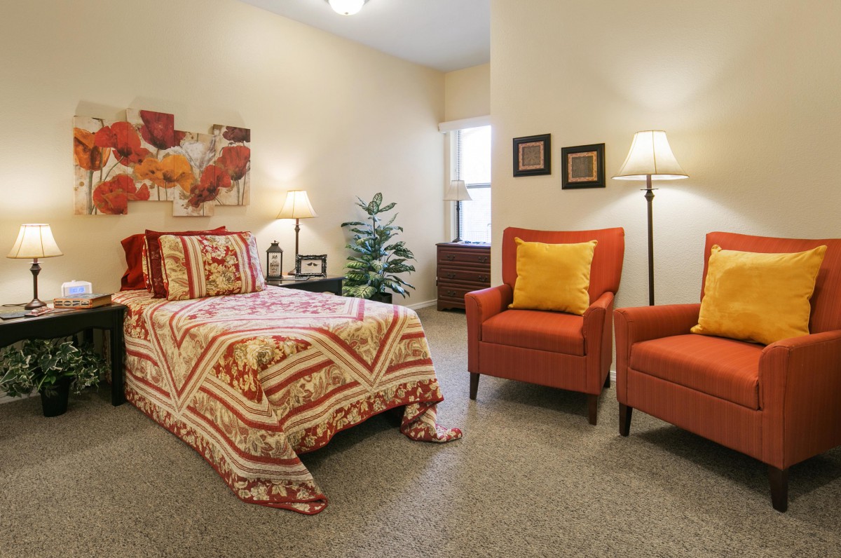 A cozy bedroom with a bed, two armchairs, and warm decor elements.