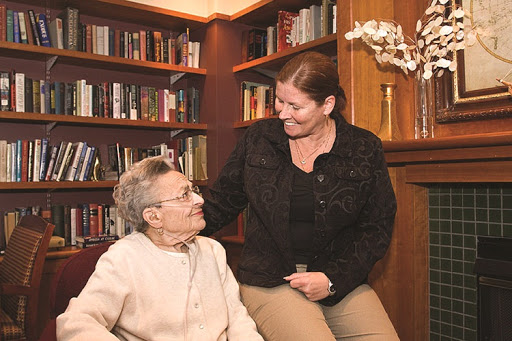 A caregiver sharing a warm moment with an elderly person in a cozy library setting.
