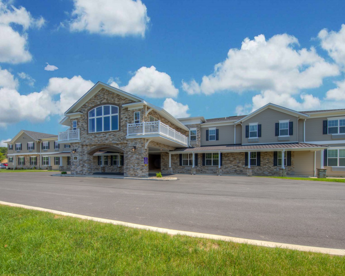 A large building with stone facade and a covered entrance under a blue sky with white clouds.