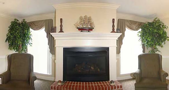 A traditional fireplace with a white mantel, adorned with a model ship and candles, set above a brick hearth.