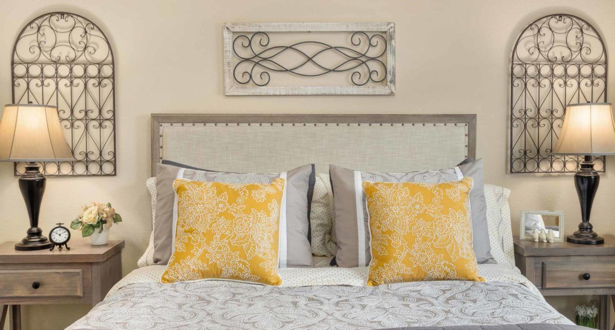 A stylish bedroom setup featuring a bed with yellow decorative pillows and a sophisticated headboard.