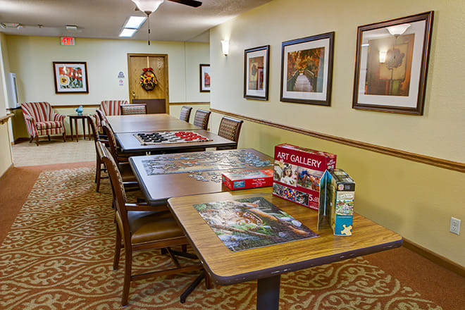 A cozy community room with tables, chairs, and puzzles set up for leisure activities.