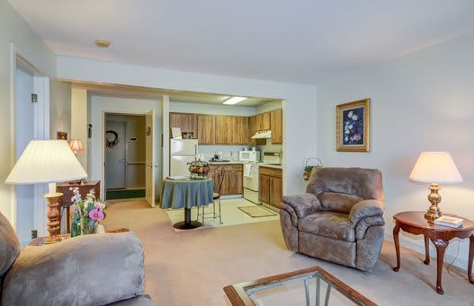 A cozy living room with an open kitchen layout, featuring comfortable armchairs and warm decor.