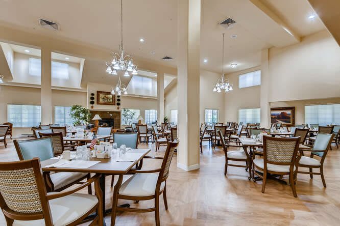A spacious and well-lit dining room with multiple tables and chairs arranged neatly, illuminated by elegant chandeliers.