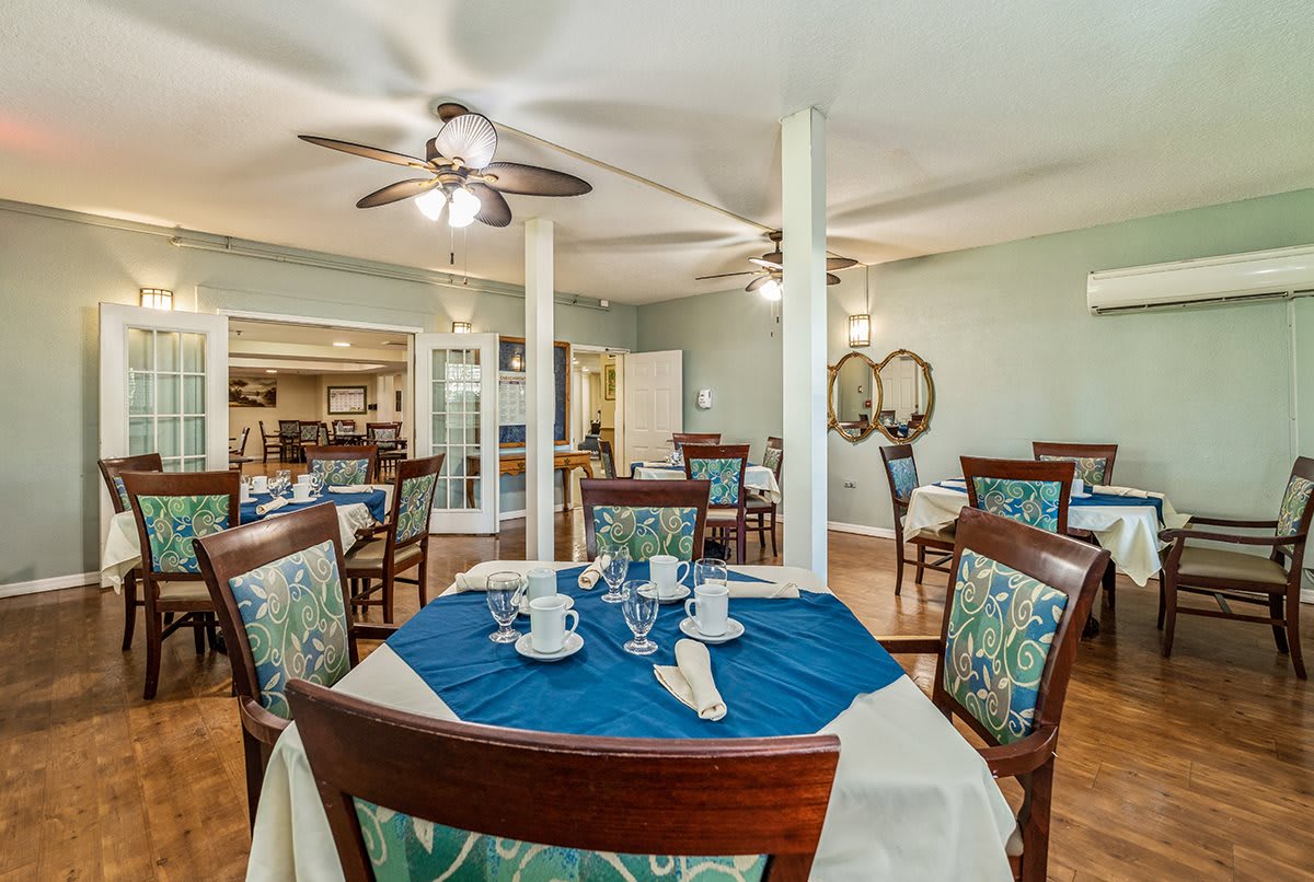 A well-decorated dining area with tables and chairs, featuring elegant place settings and ceiling fans.