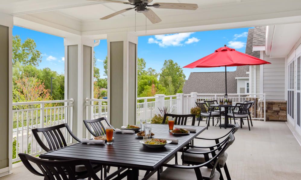 A cozy outdoor patio with a dining area, featuring a table set for a meal and a red umbrella providing shade.