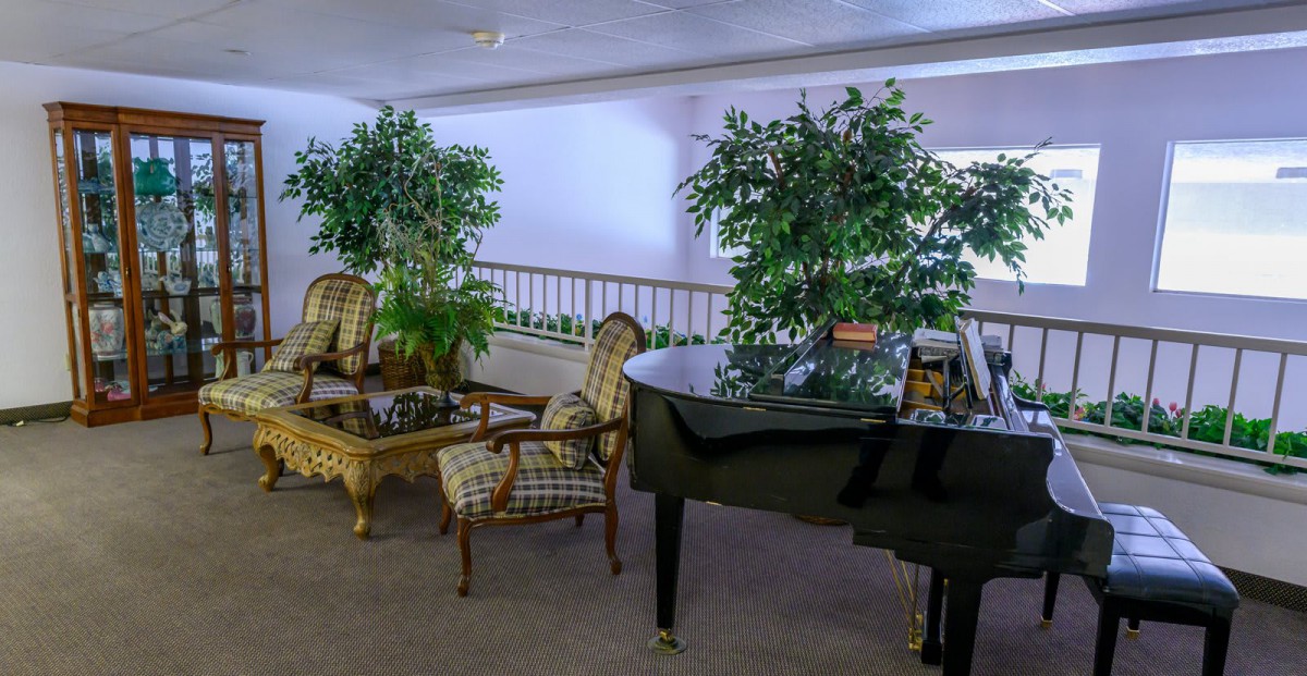 A cozy lobby area featuring a grand piano, elegant chairs, and lush indoor plants.