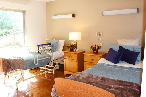 A well-lit hospital room featuring two beds and bedside furniture.