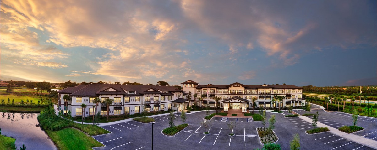 A modern residential complex with a spacious parking lot under a cloudy sunset sky.