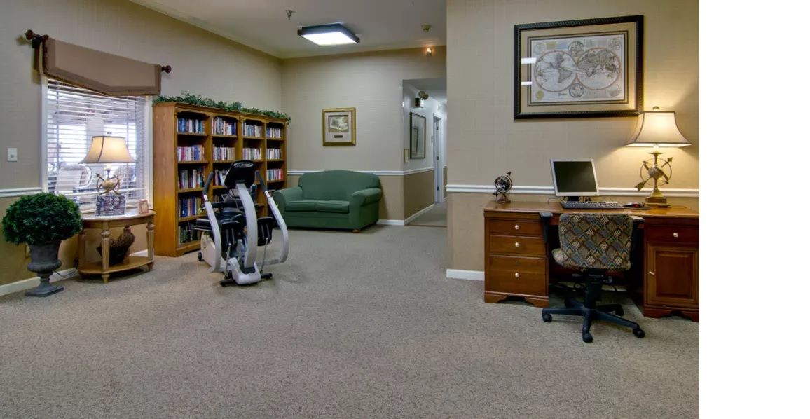 An office space featuring a desk with a laptop, a sofa, bookshelves, and exercise equipment.
