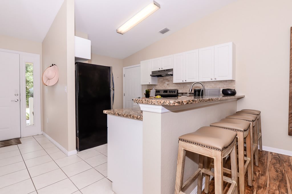 A modern kitchen with white cabinets, granite countertops, and bar stools.