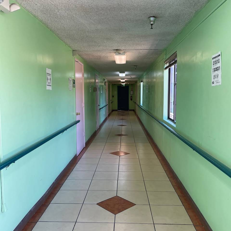 A long, well-lit hospital corridor with green walls and tiled flooring.