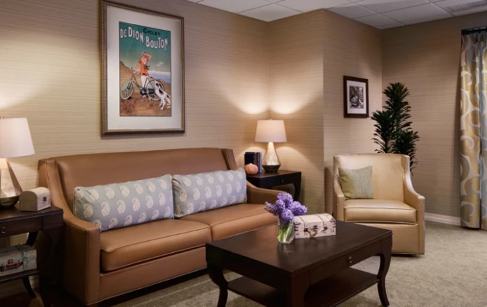 A cozy living room with a sofa, armchair, and coffee table, decorated with artwork and a lamp.