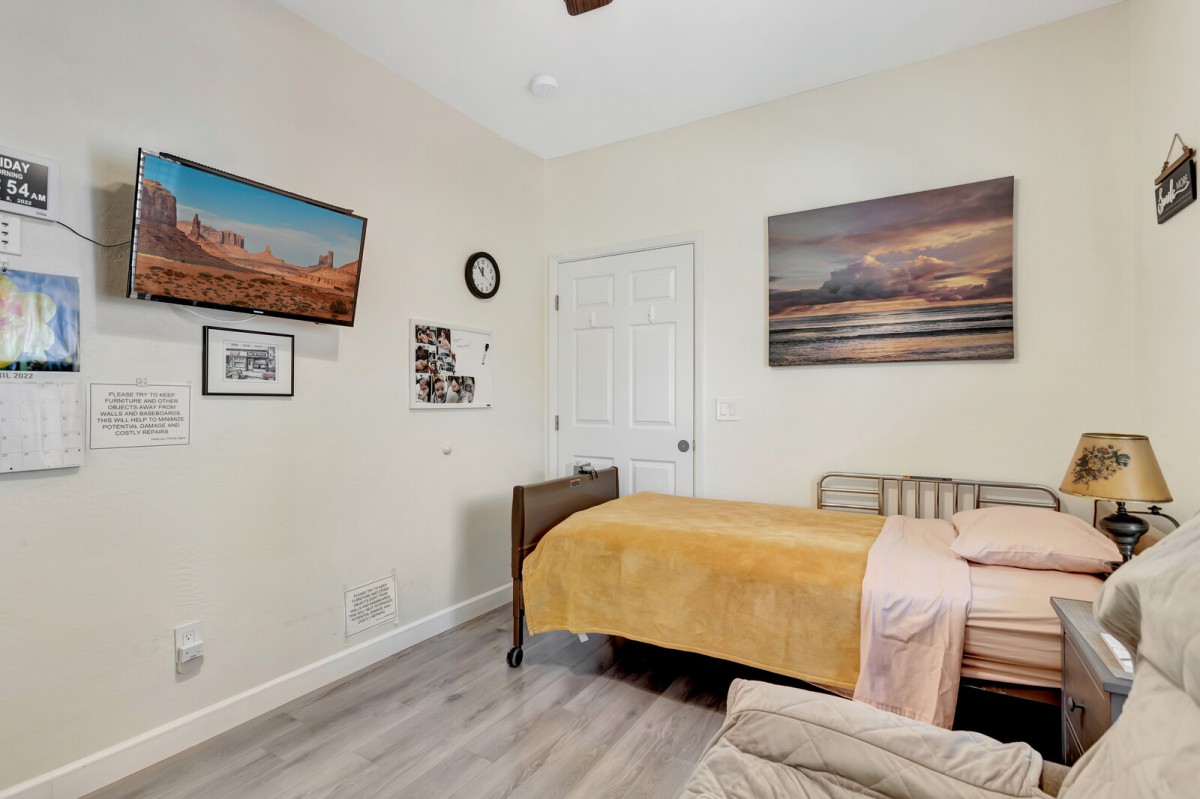 A cozy bedroom featuring a bed with a yellow blanket, wall art, and light wood flooring.