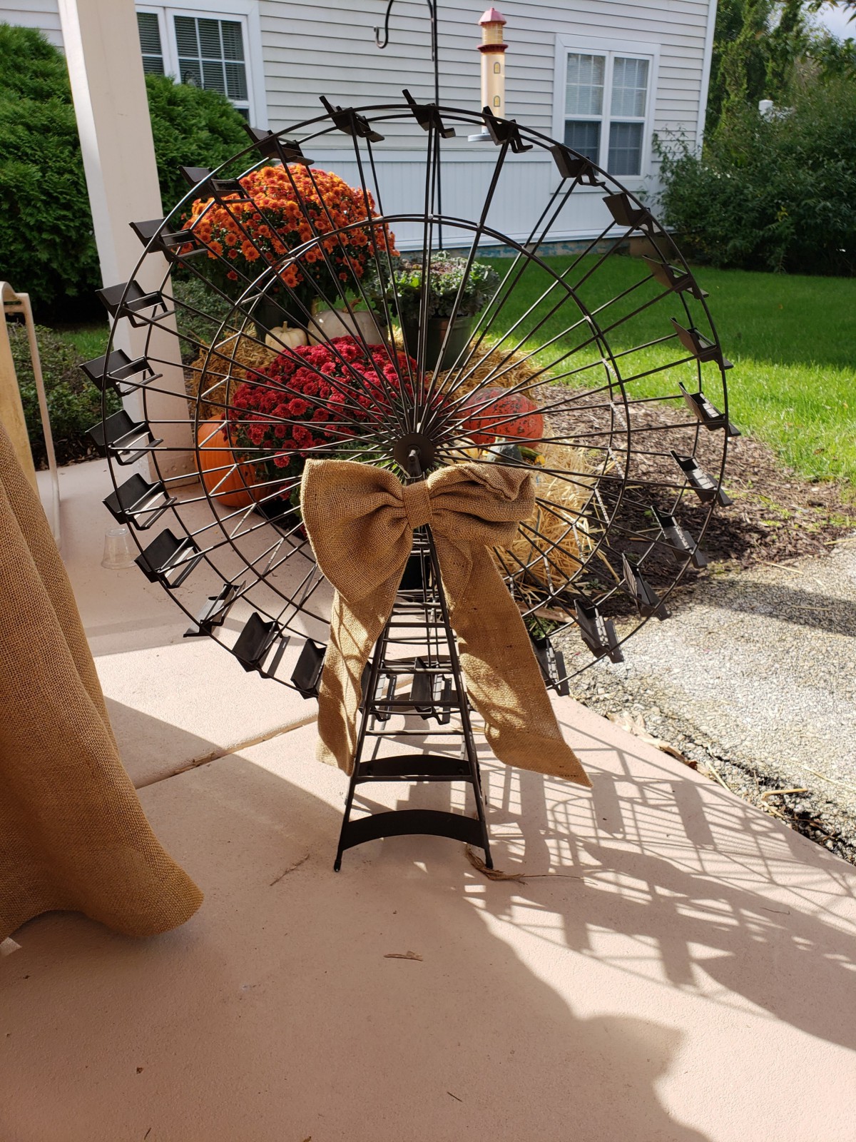A decorative Ferris wheel adorned with autumn flowers and a burlap bow, set in an outdoor space.