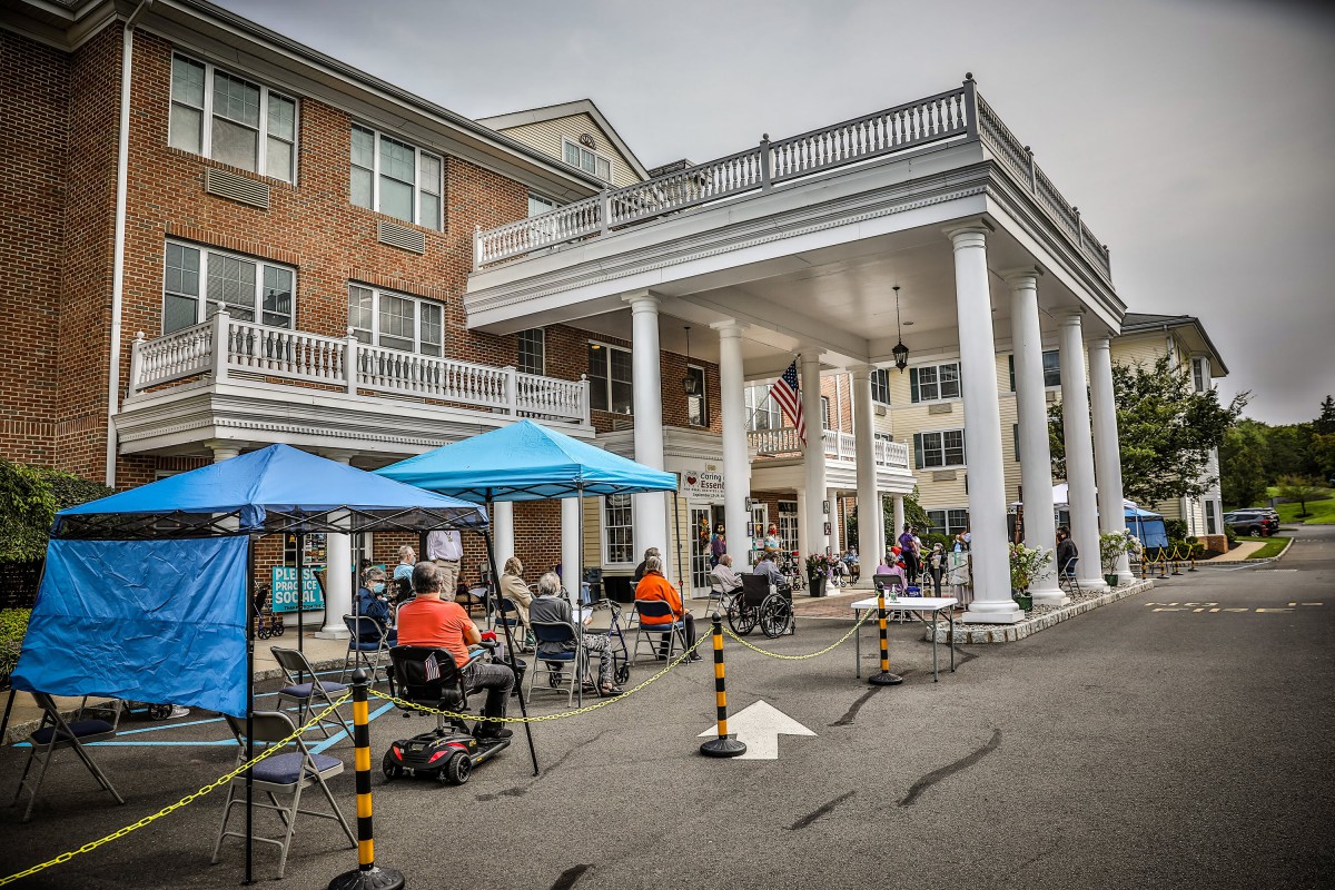 An outdoor event in front of a building with large columns, featuring tents, tables, and chairs.